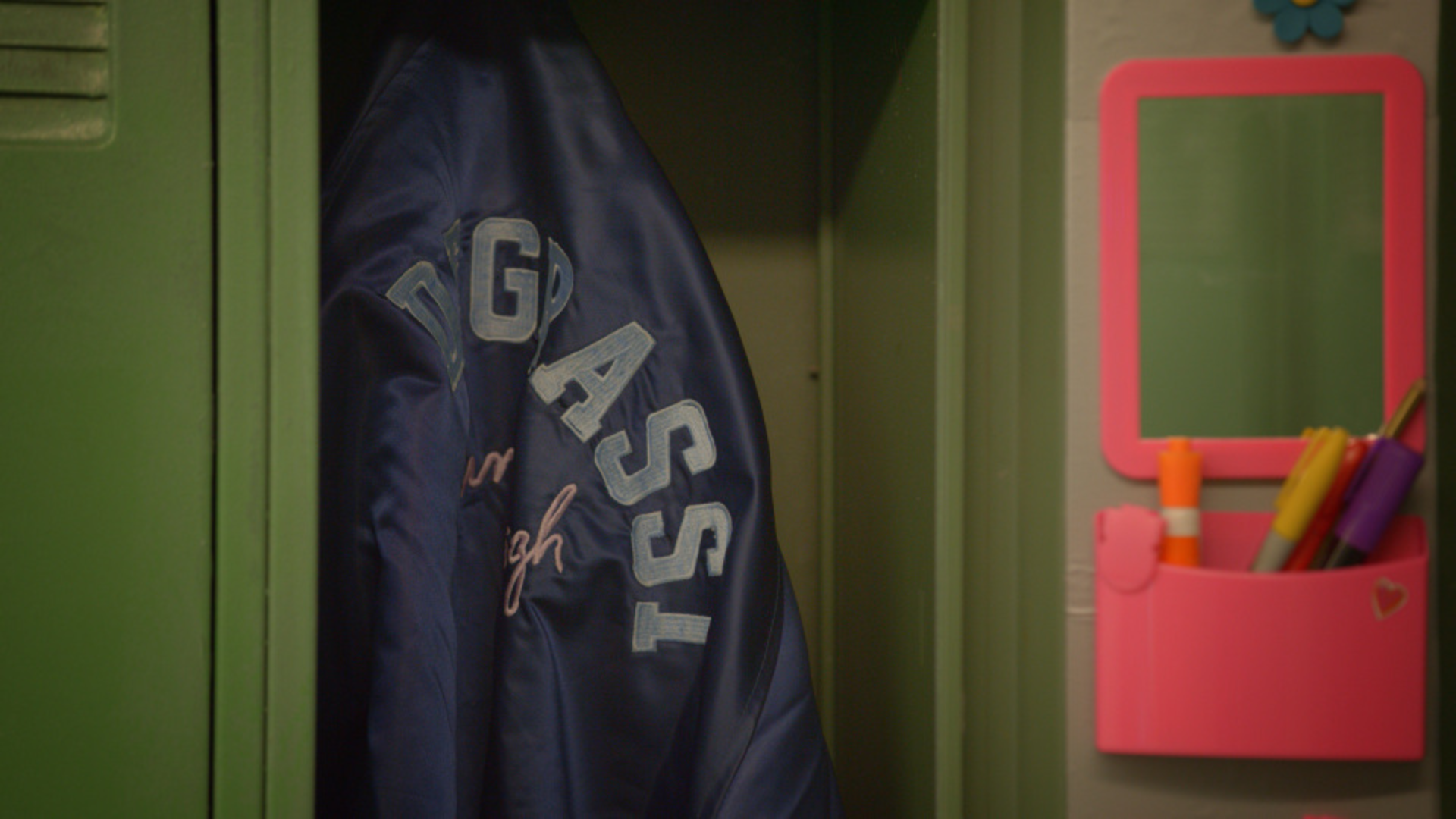 a navy blue varsity jacket with the text 'Degrassi' on the back hanging in a green locker