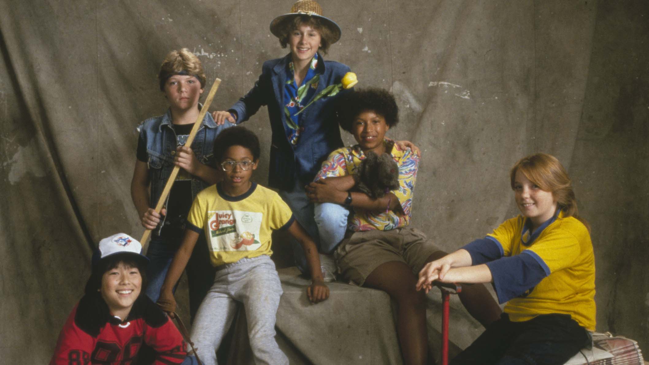 A group of young kids from the 1970s, posing for a photo in front of a beige photography backdrop.